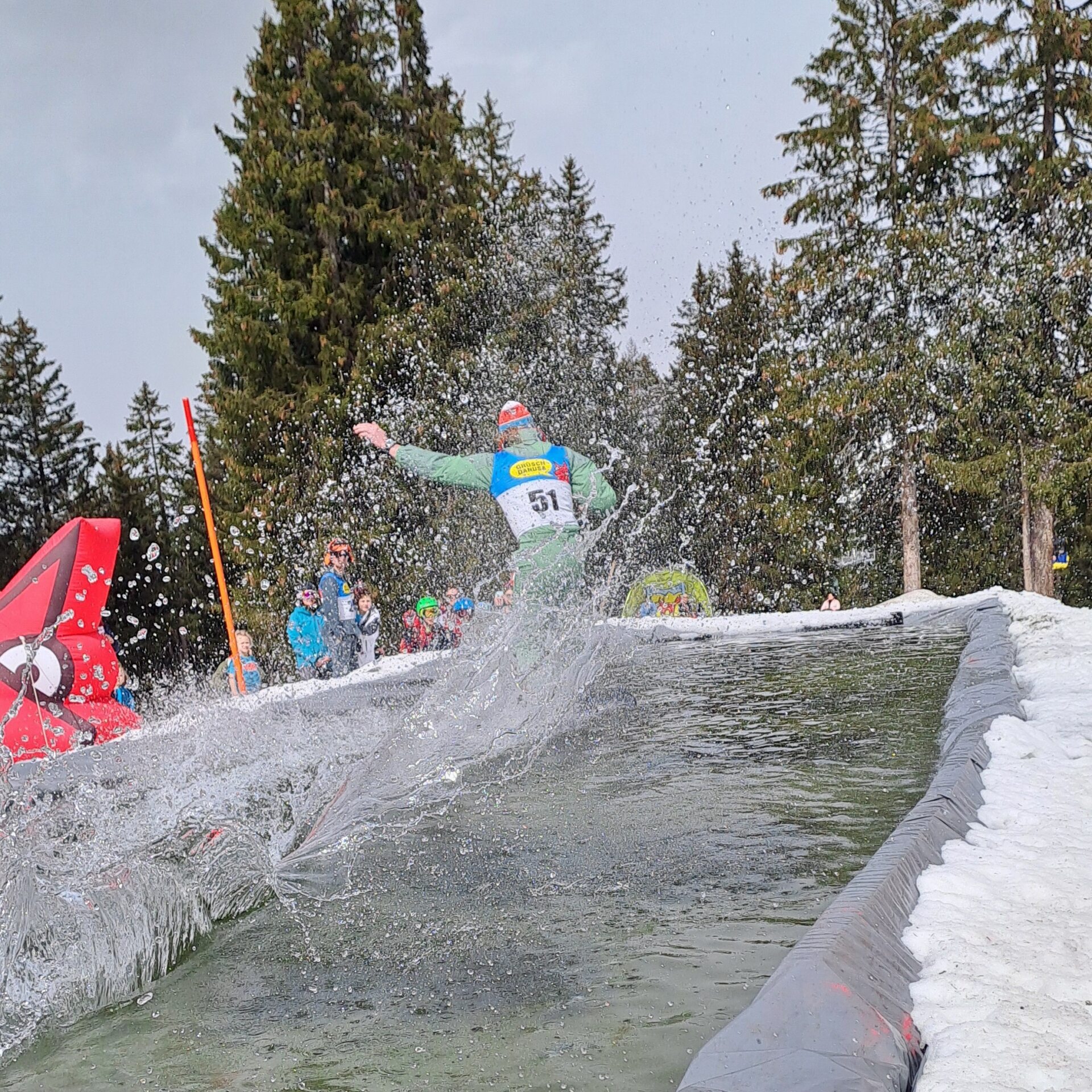 Snowboarder fährt über das Wasser am Waterslide, Wasser spritzt in alle Richtungen