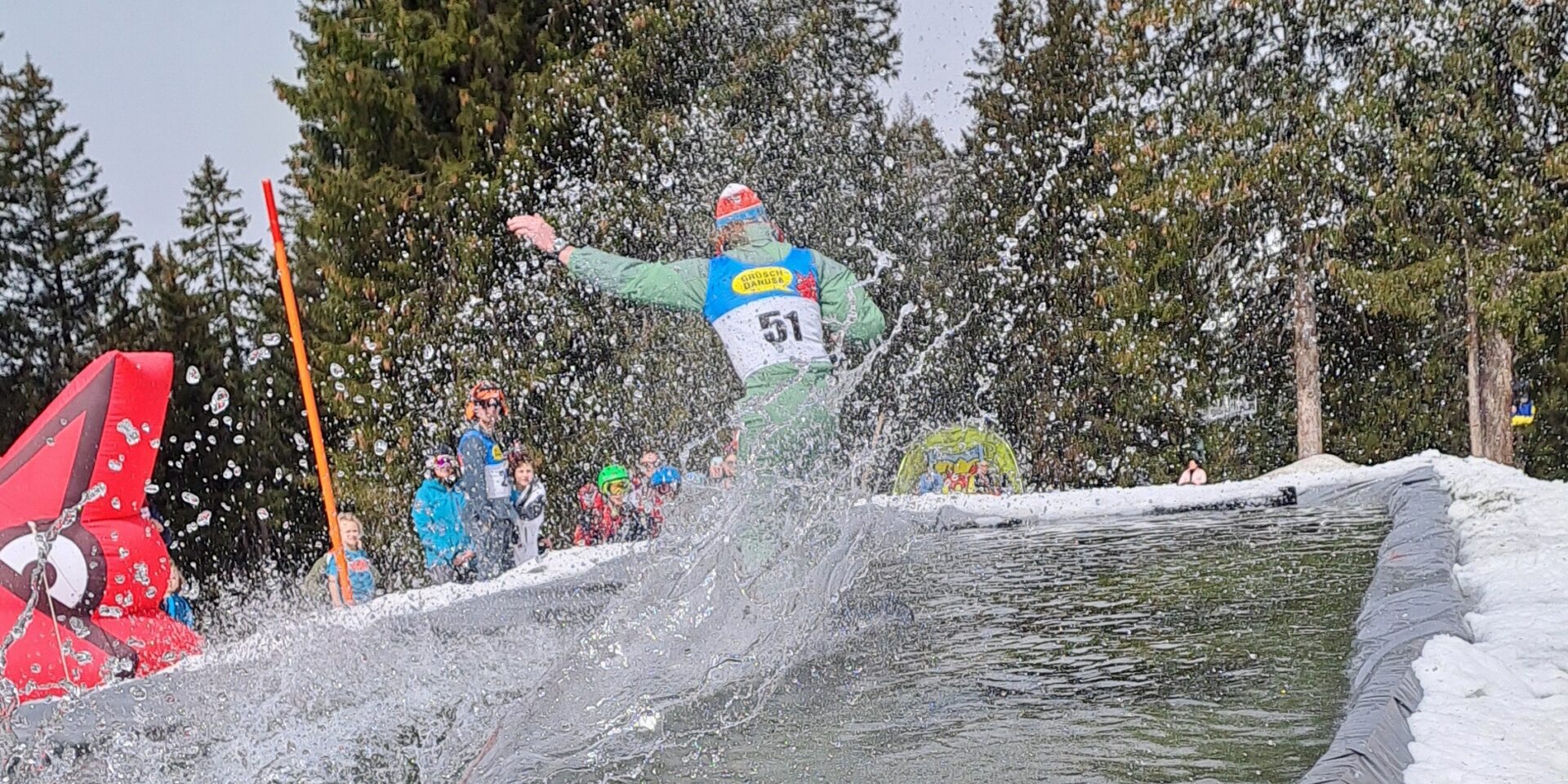 Snowboarder fährt über das Wasser am Waterslide, Wasser spritzt in alle Richtungen