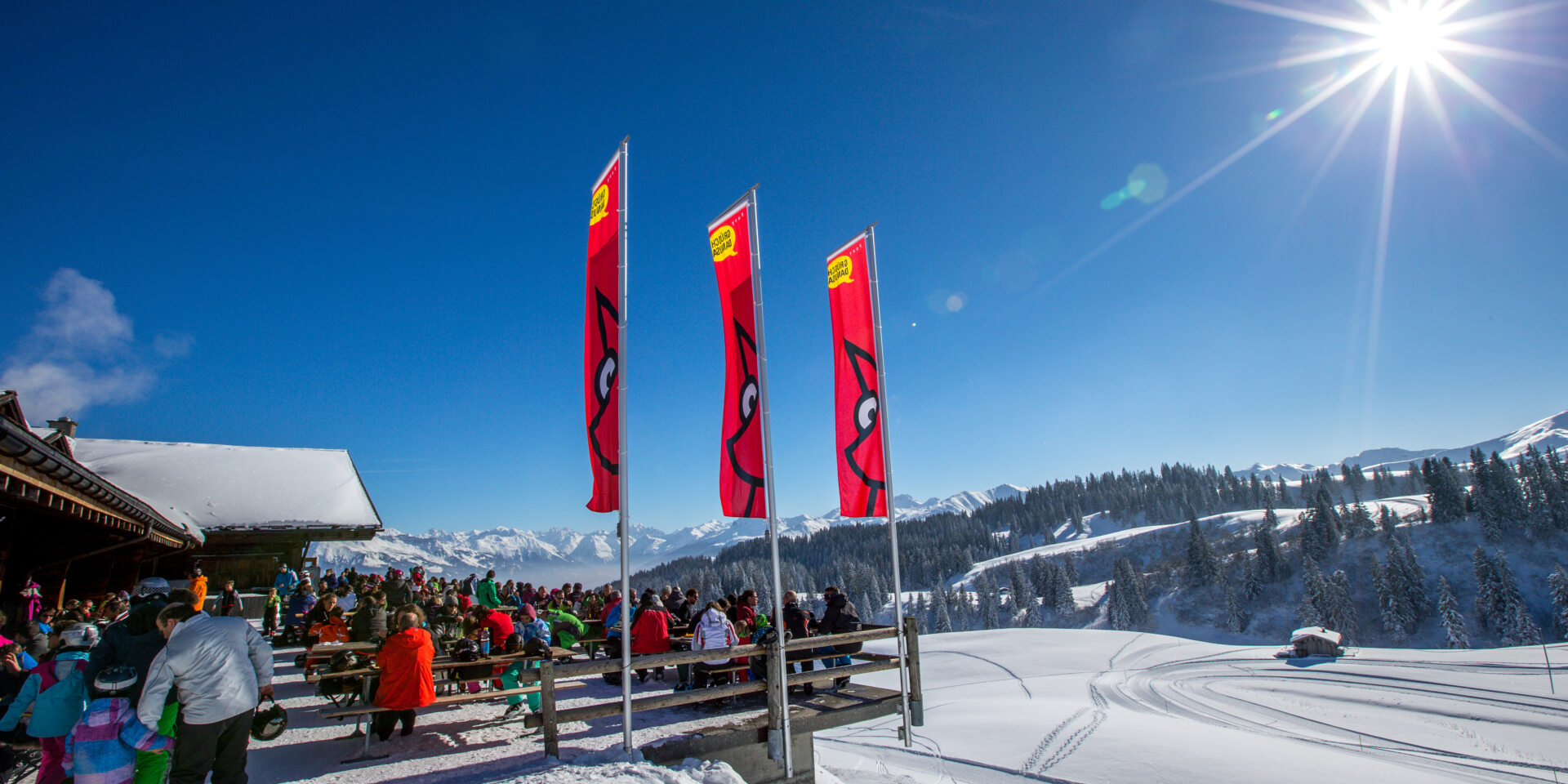 Blick aus der Distanz auf die volle Berghaus Terrasse mit Panorama