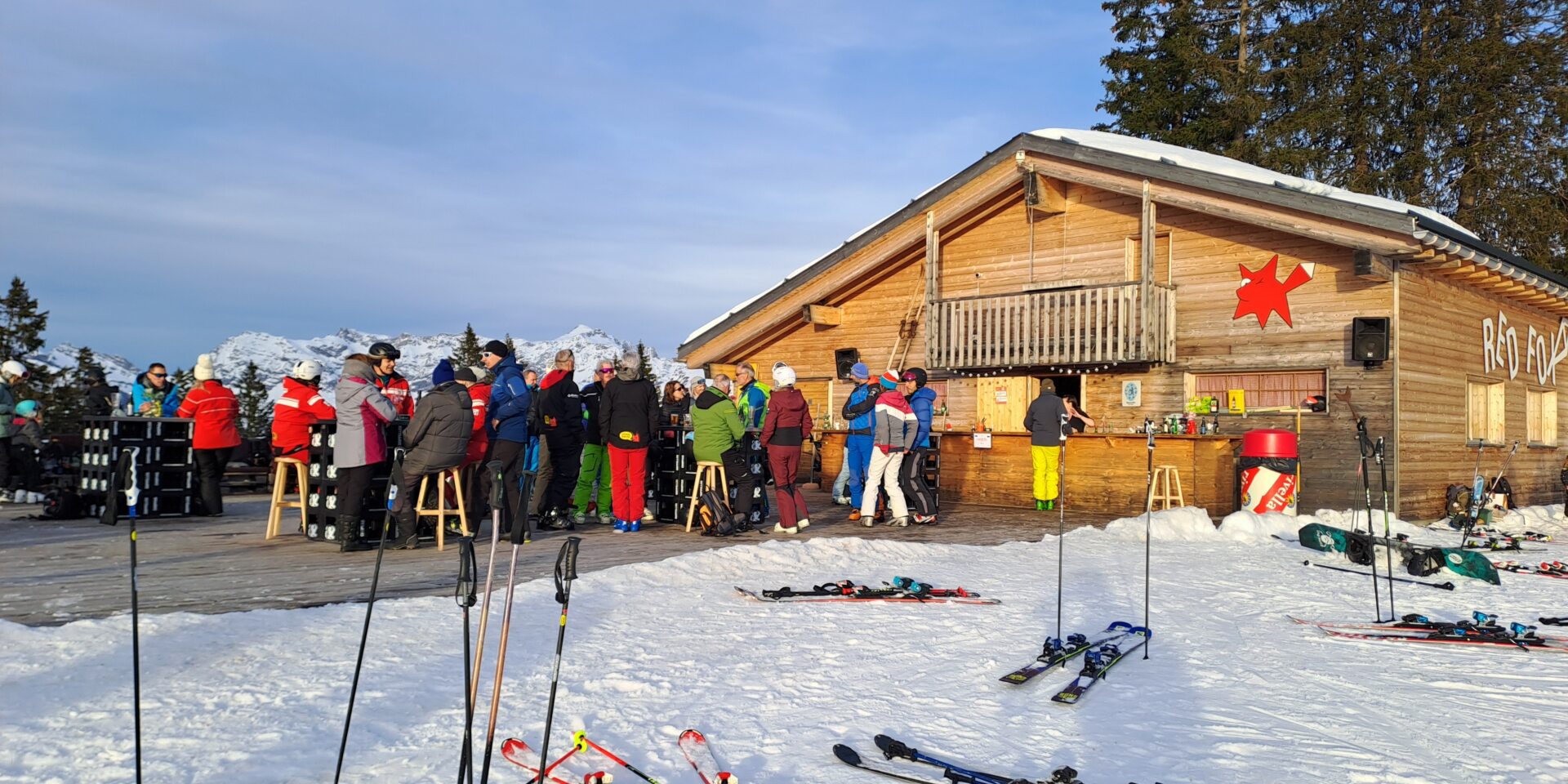 Red Fox Terasse mit Leuten und Ski mit Stöcken im Vordergrund