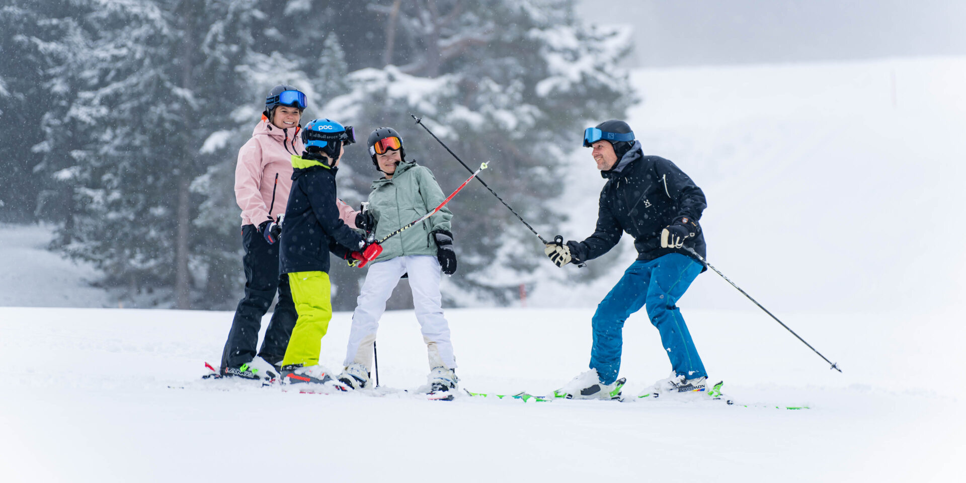 Vater und Sohn kaempfen mit den Skistoecken Mutter und Tochter schauen im Hintergrund zu alle lachen