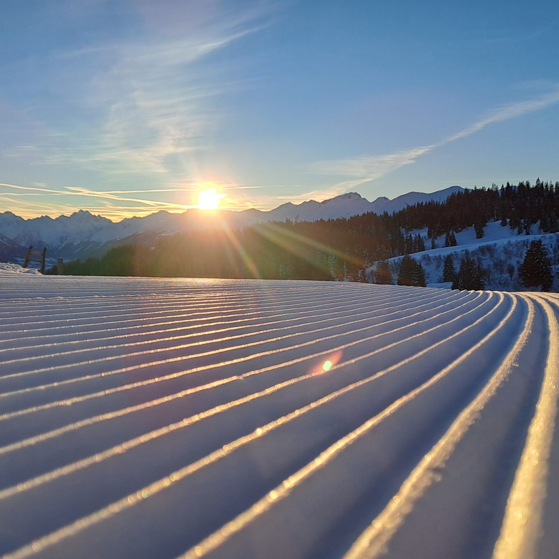 Frisch präparierte Piste mit den ersten Sonnenstrahlen über den Bergen