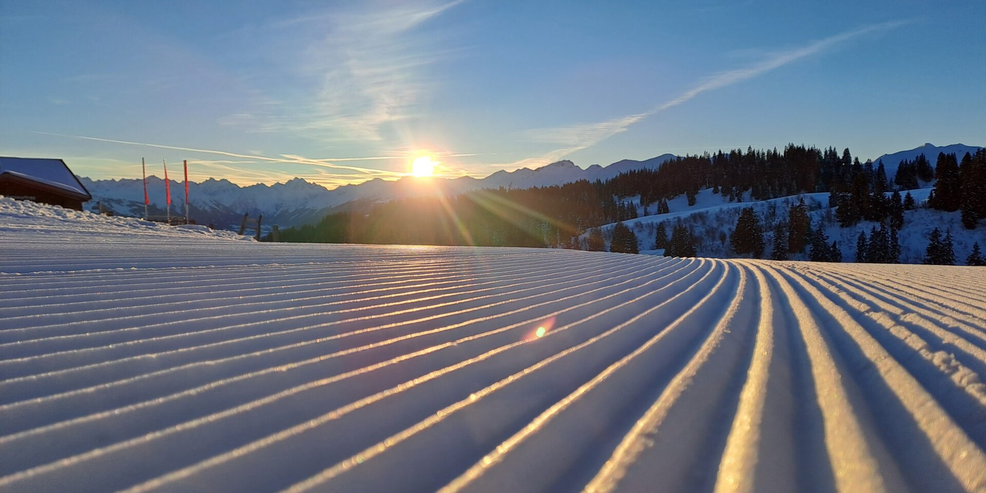 Frisch präparierte Piste mit den ersten Sonnenstrahlen über den Bergen