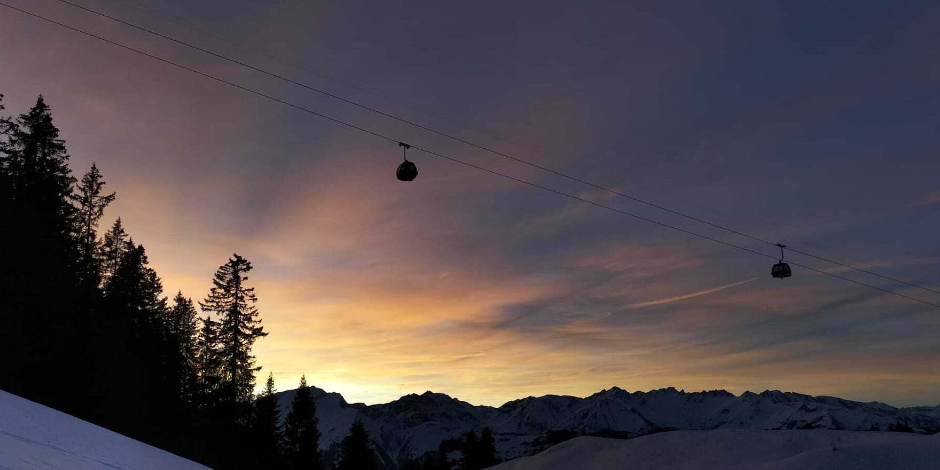 Zwei Gondelbahnen hoch vor dem farbigen Himmel