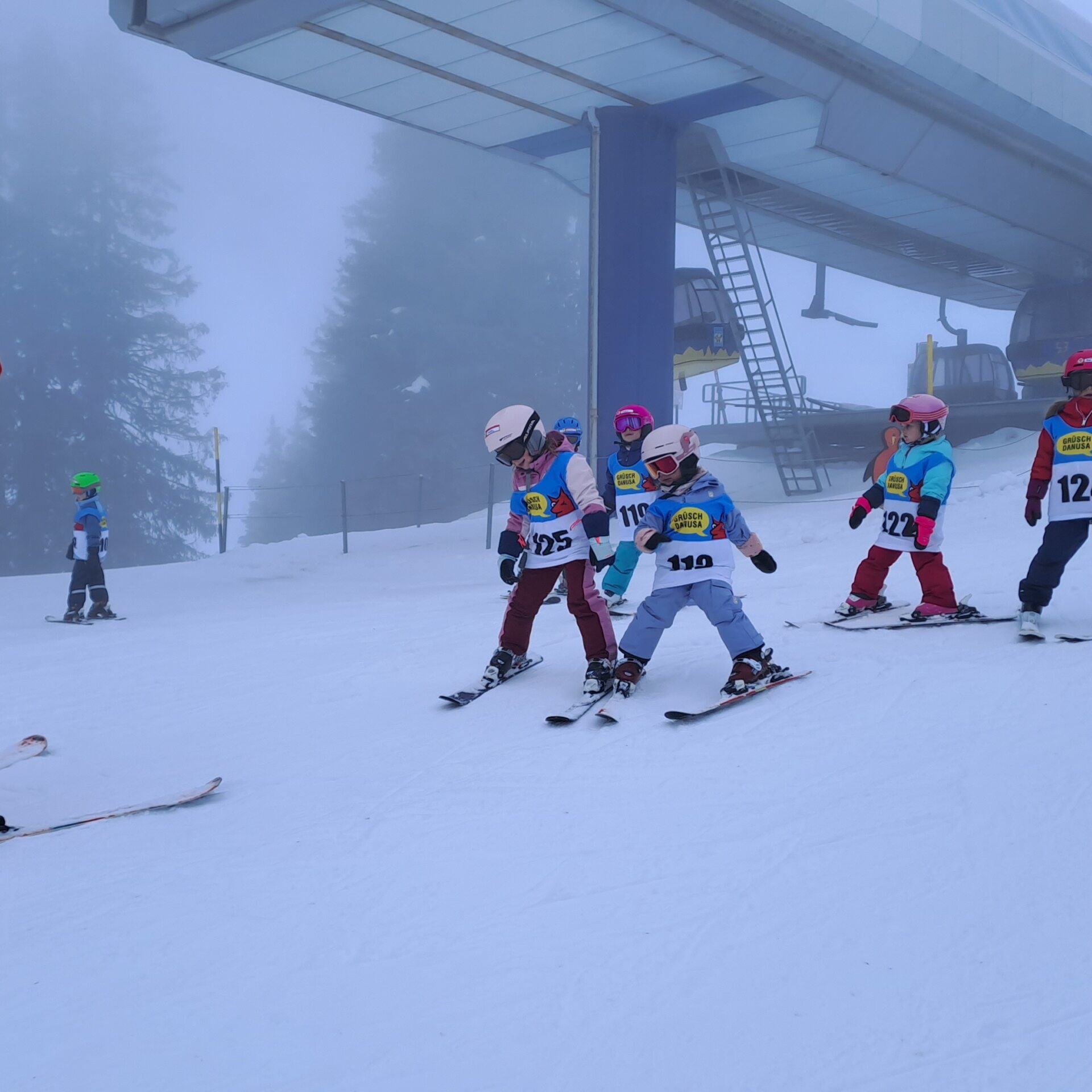 Skilehrerin steht unten am der Piste, Kinder vor ihr und sie spielen Sonne, Mond und Sterne