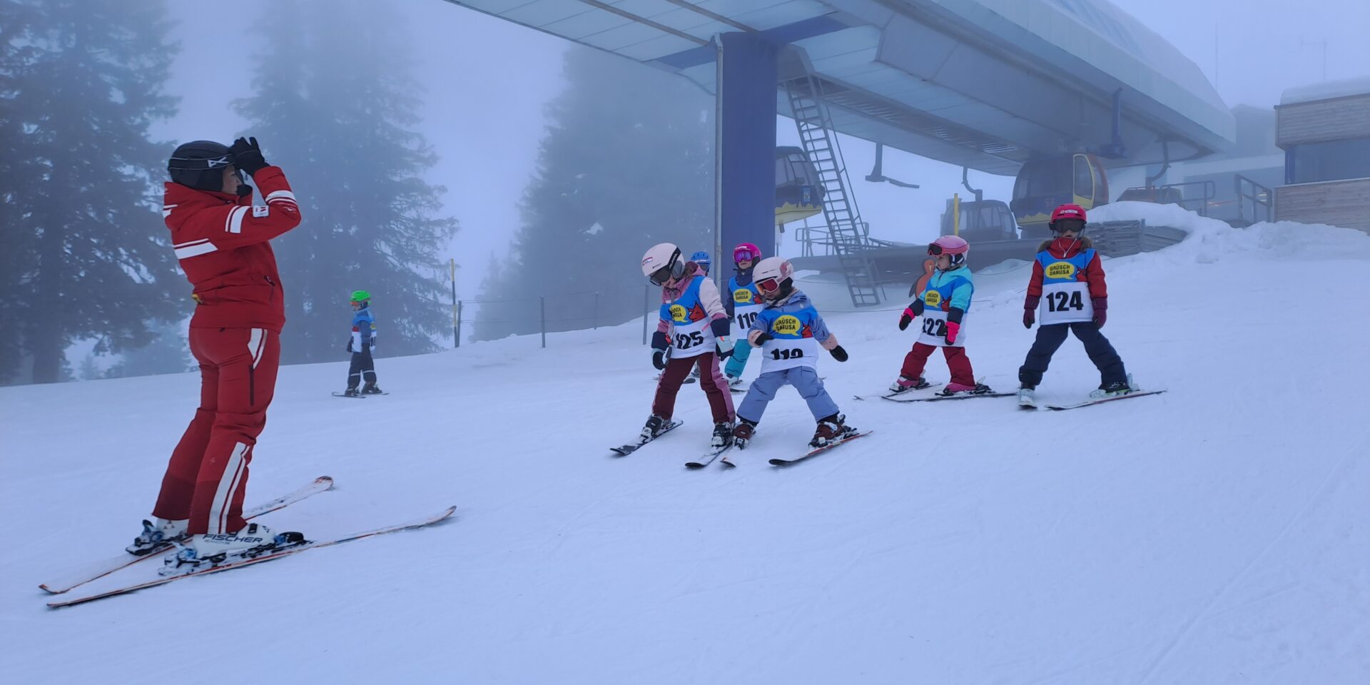 Skilehrerin steht unten am der Piste, Kinder vor ihr und sie spielen Sonne, Mond und Sterne