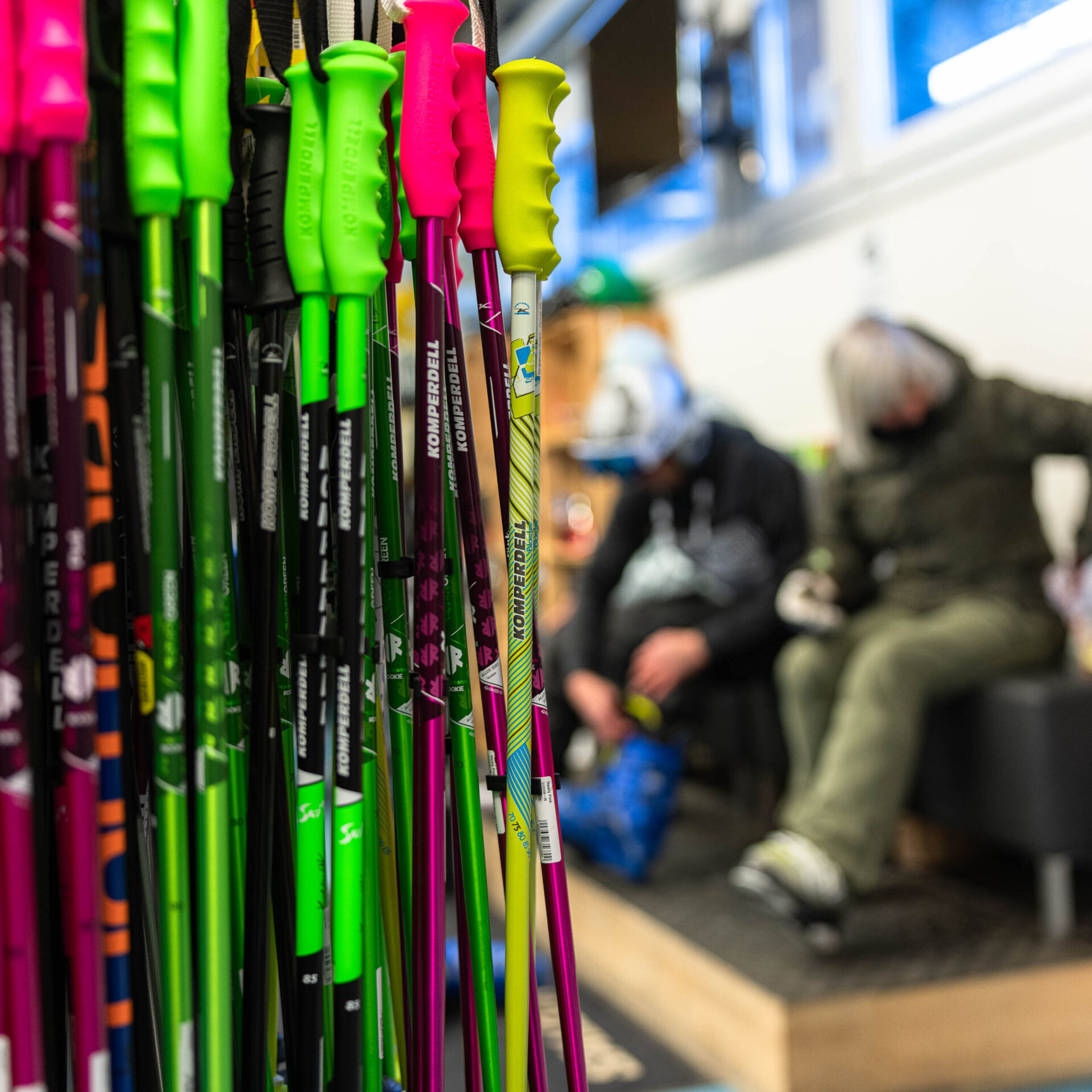 Gestell mit Skistöcken links im Fokus im Hintergrund Skifahrer die ihr Material