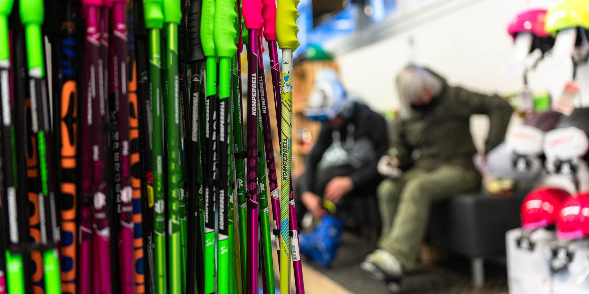 Gestell mit Skistöcken links im Fokus im Hintergrund Skifahrer die ihr Material