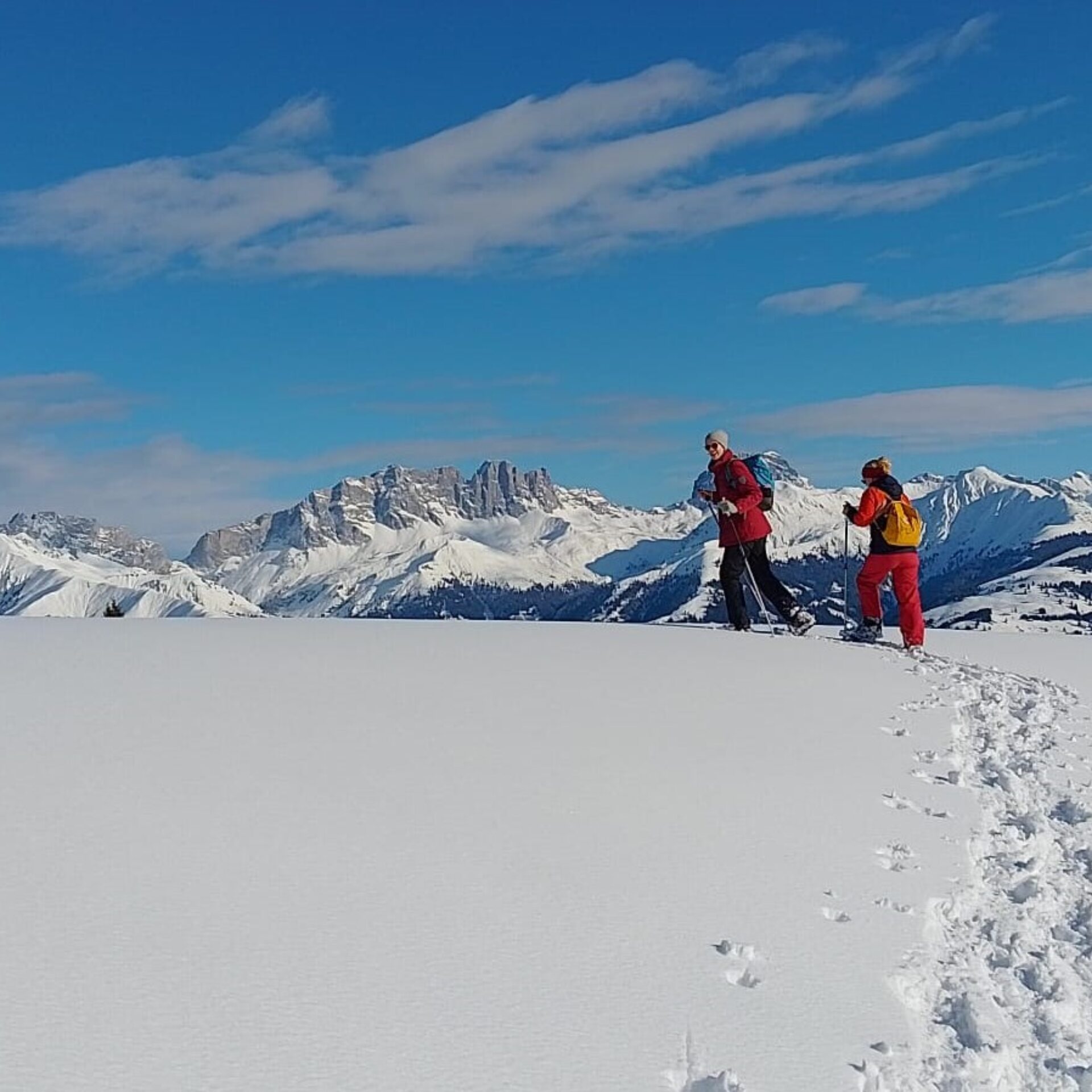 Zwei Frauen laufen vor der Bergkulisse, hinter ihnen die Schneespuren