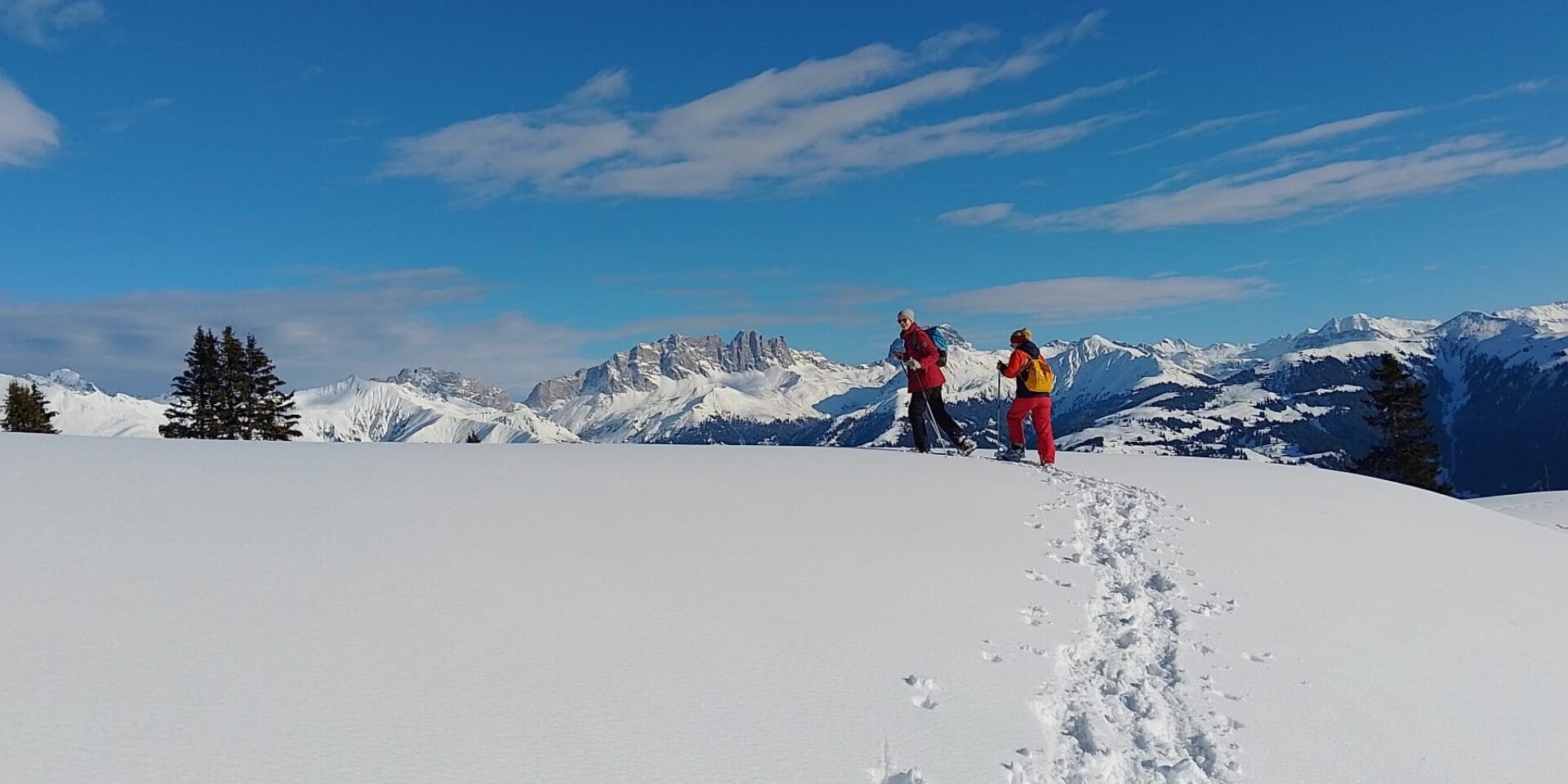 Zwei Frauen laufen vor der Bergkulisse, hinter ihnen die Schneespuren