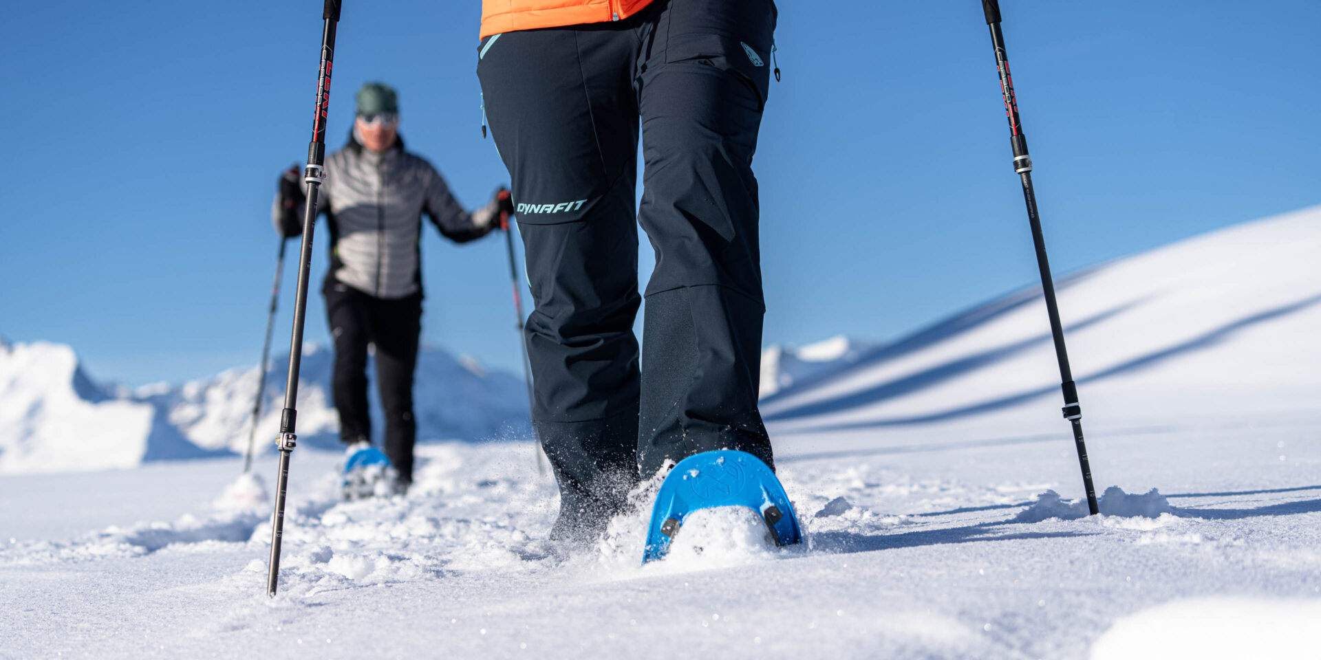 Vorne eine Schneeschuhlaeuferin von der Huefte abwaerts im Hintergrund ein zweiter Schneeschuhlaeufer im Ganzkoerperbild