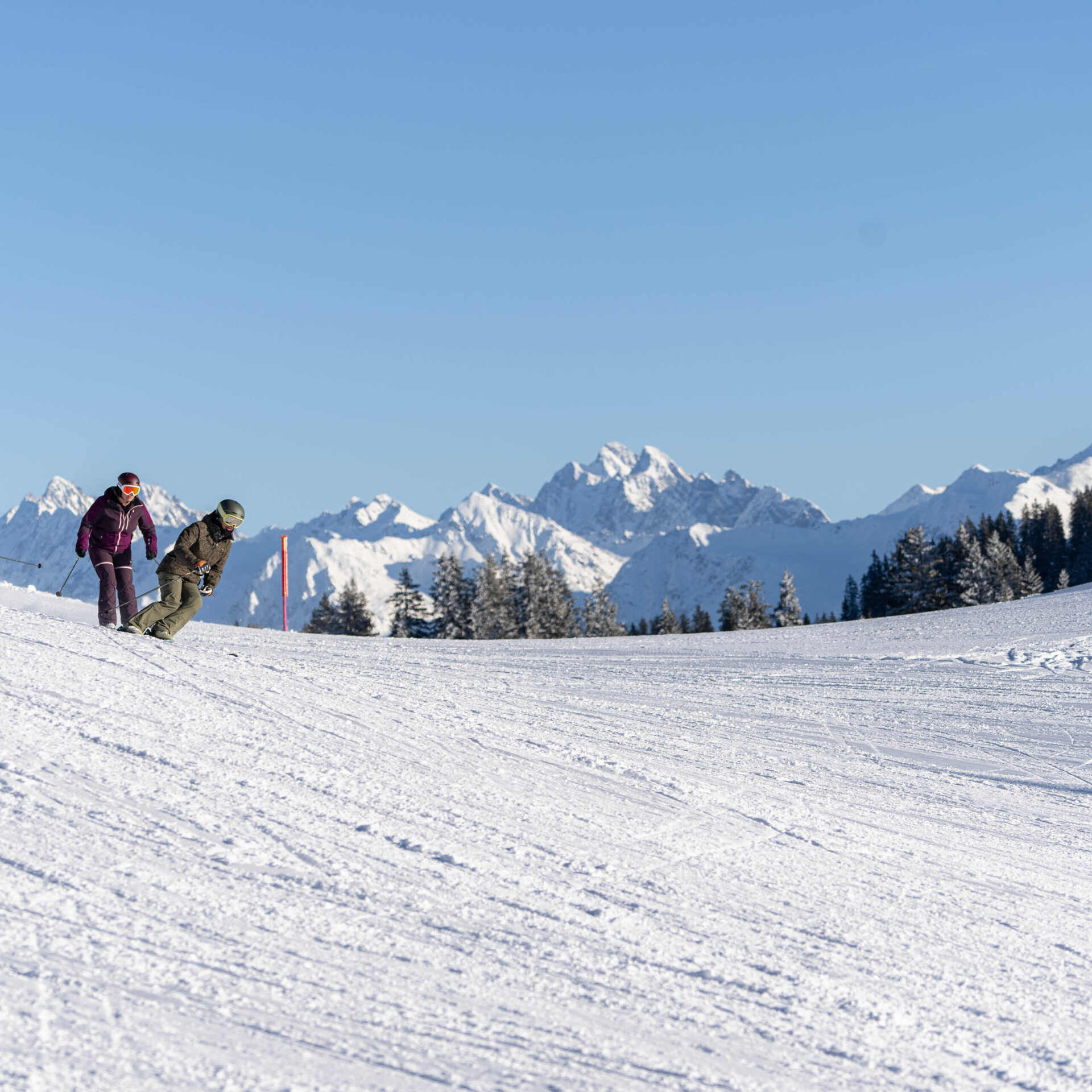 Drei Skifahrer auf der Piste vor einer Bergkette