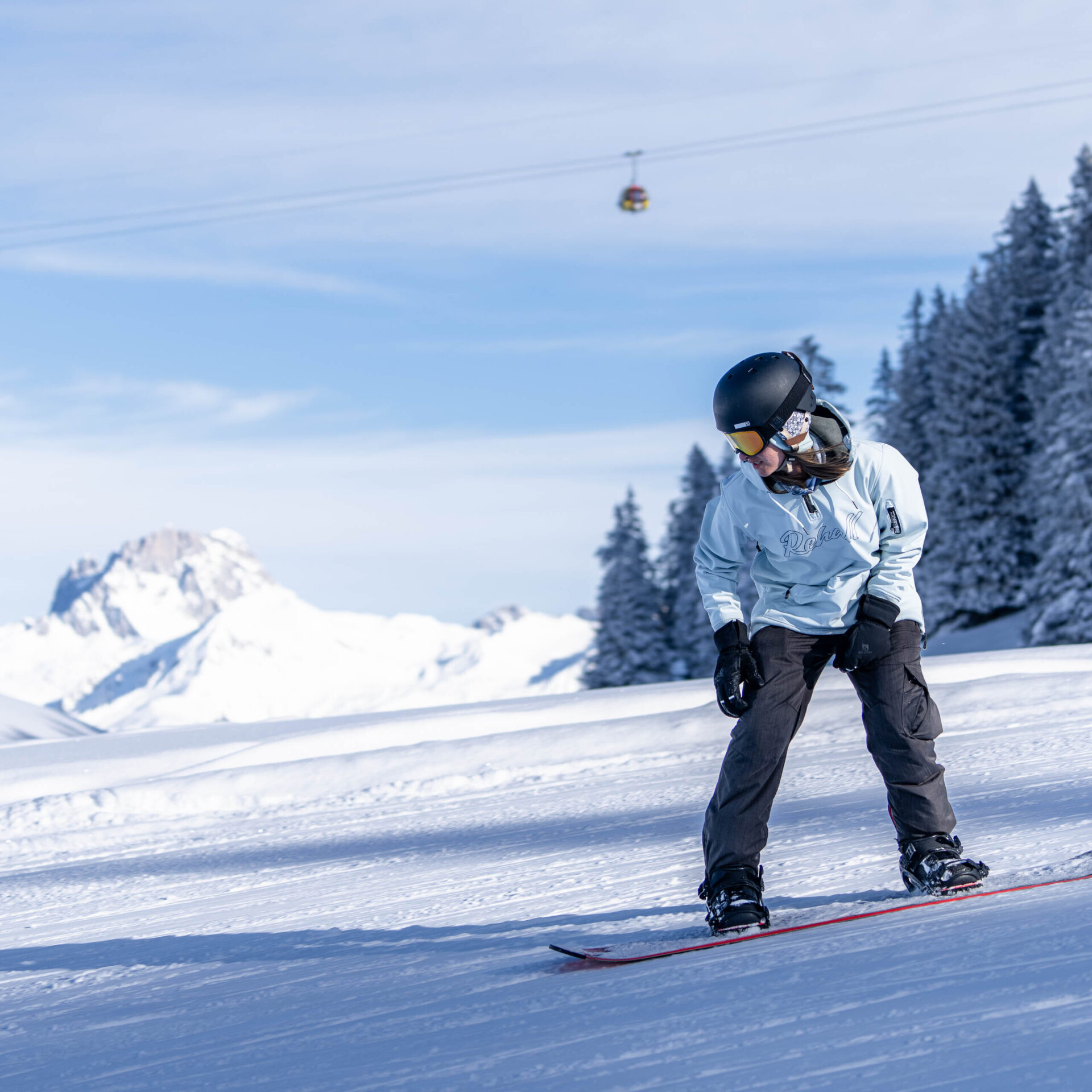 Snowboarderin in der Hocke klein im Hintergrund die Gondelbahn