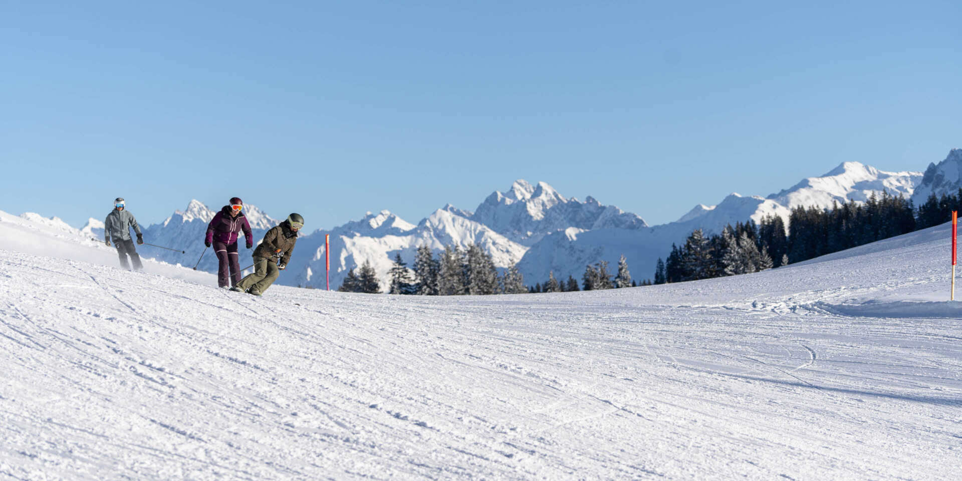 Drei Skifahrer auf der Piste vor einer Bergkette