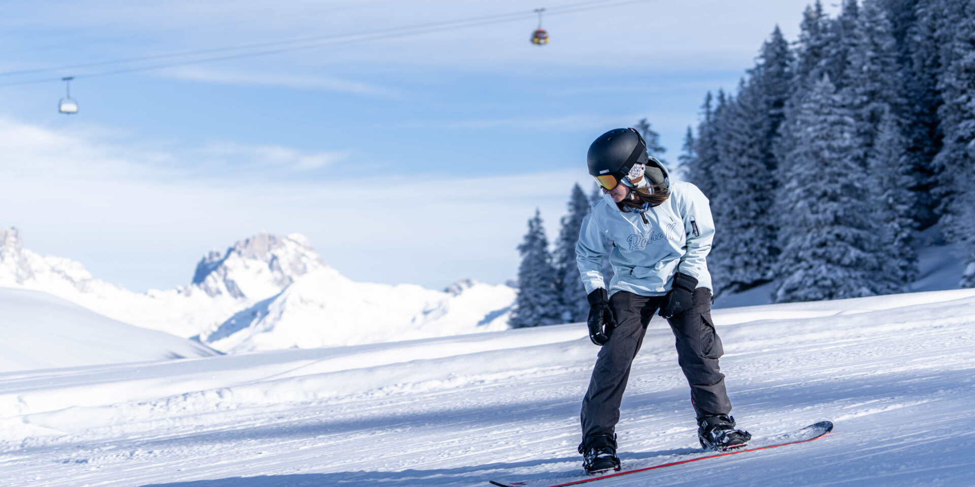 Snowboarderin in der Hocke klein im Hintergrund die Gondelbahn