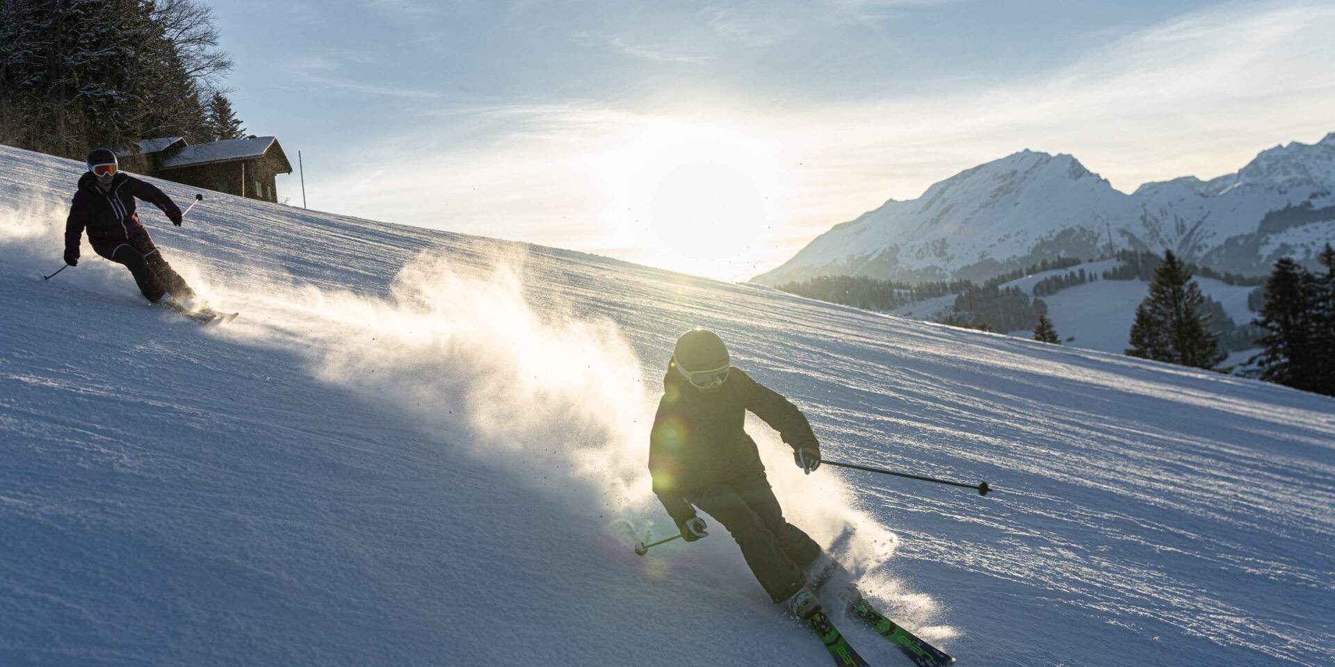 Zwei Skifahrerinnen in der Sonne mit aufgewirbeltem Schnee