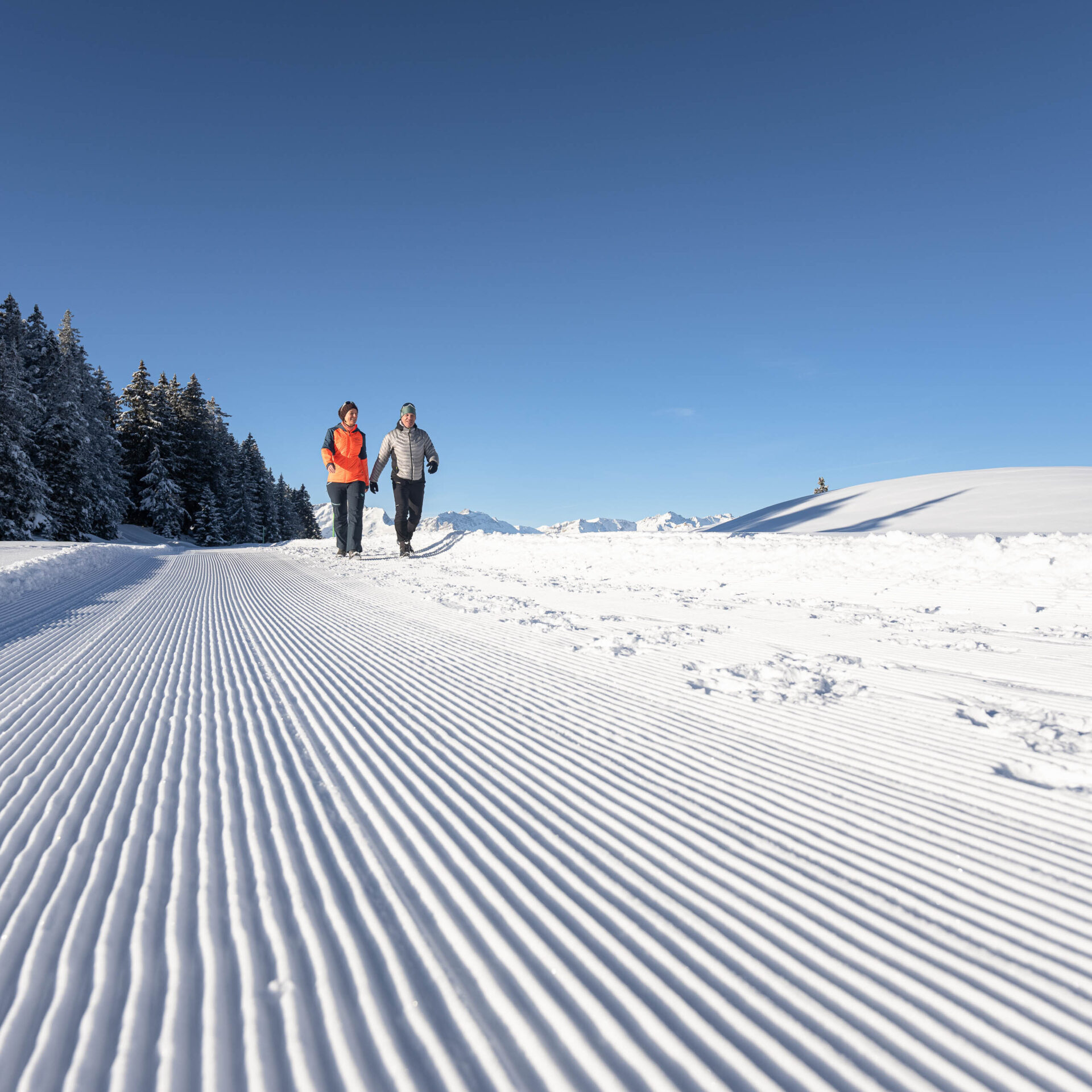 Zwei Winterwanderer auf frisch praeparierten Pisten am Morgen unterwegs