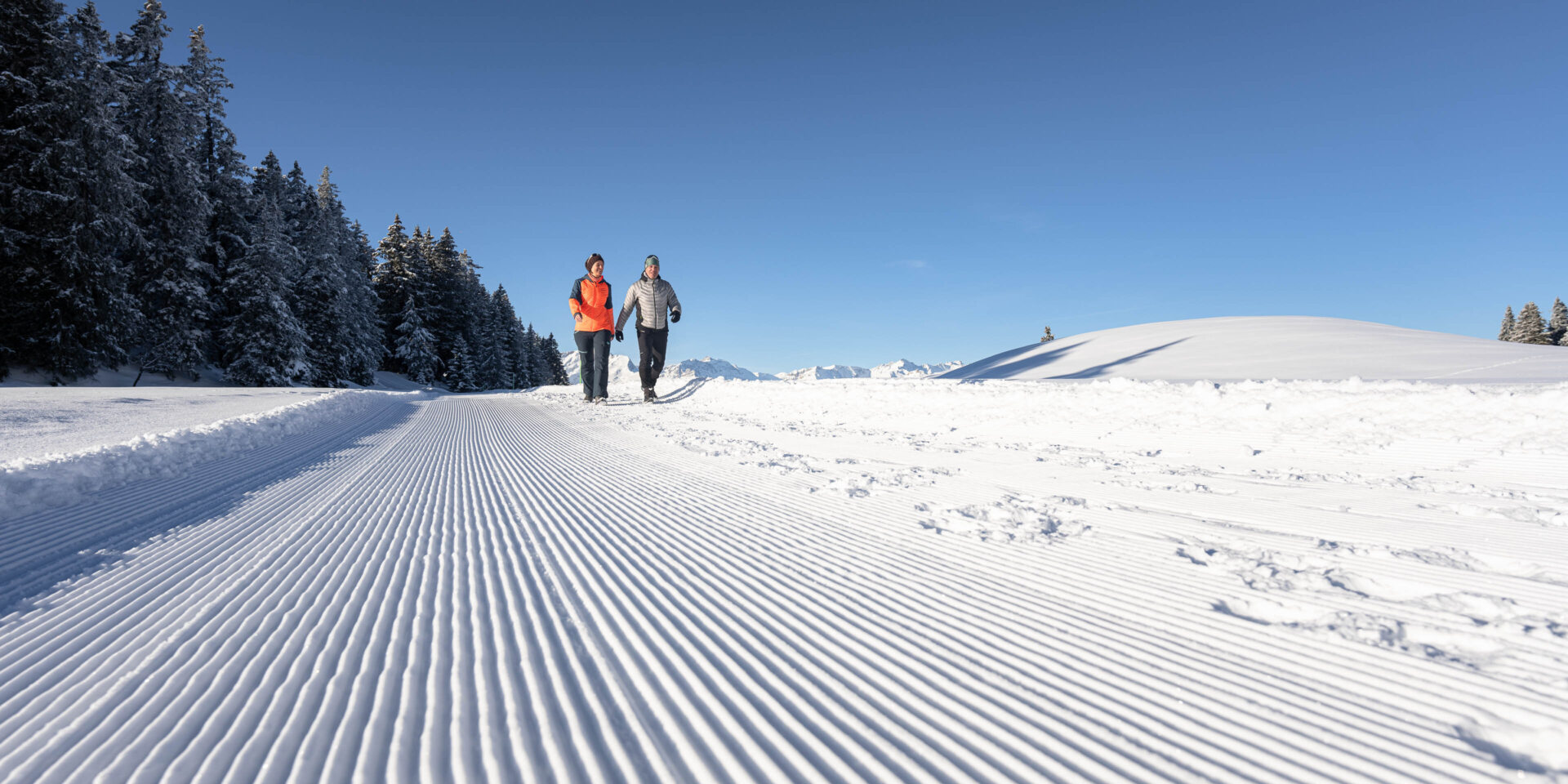 Zwei Winterwanderer auf frisch praeparierten Pisten am Morgen unterwegs