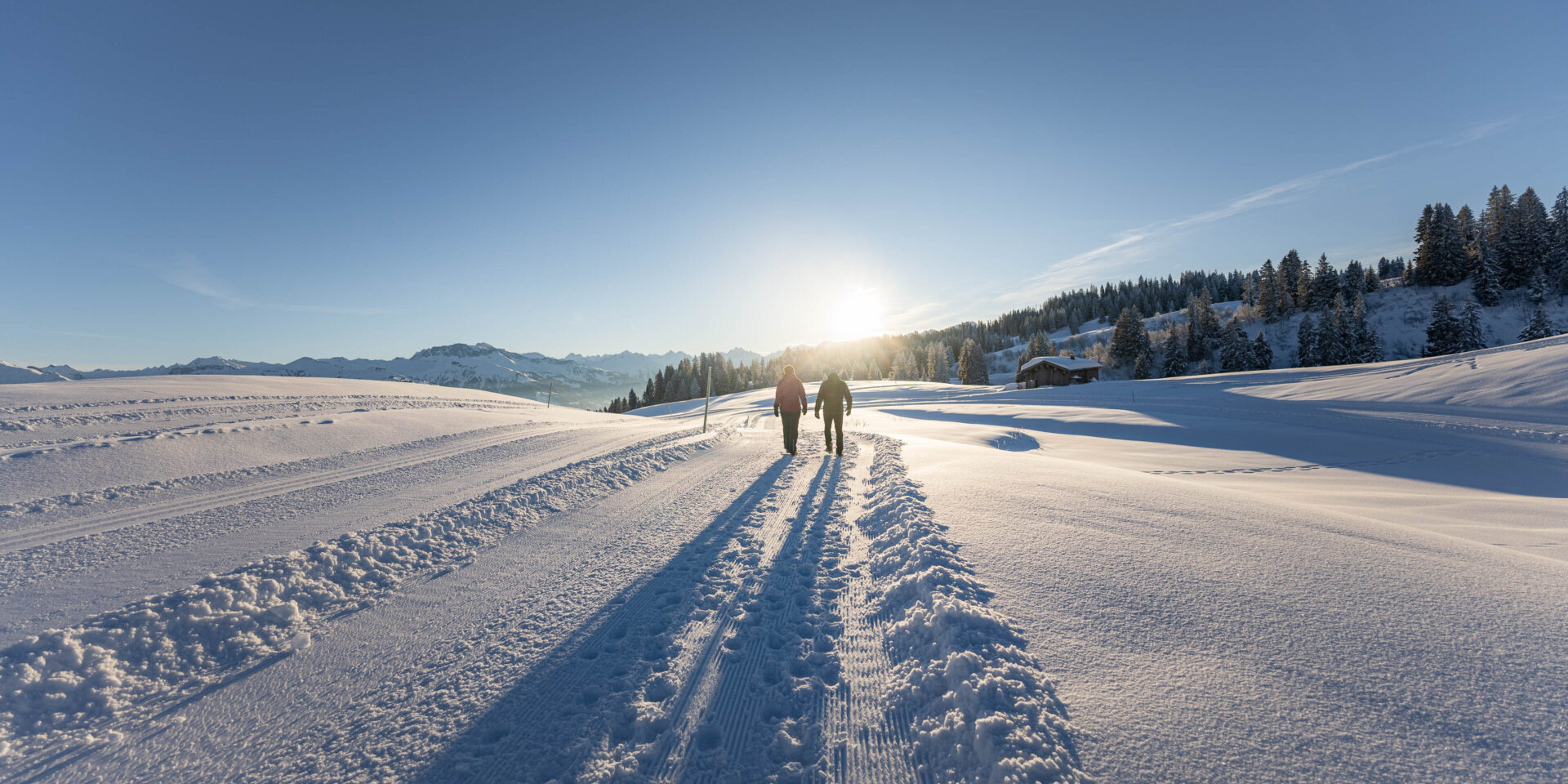 Zwei Winterwanderer vor der aufgehenden Sonne in der Ferne am Laufen