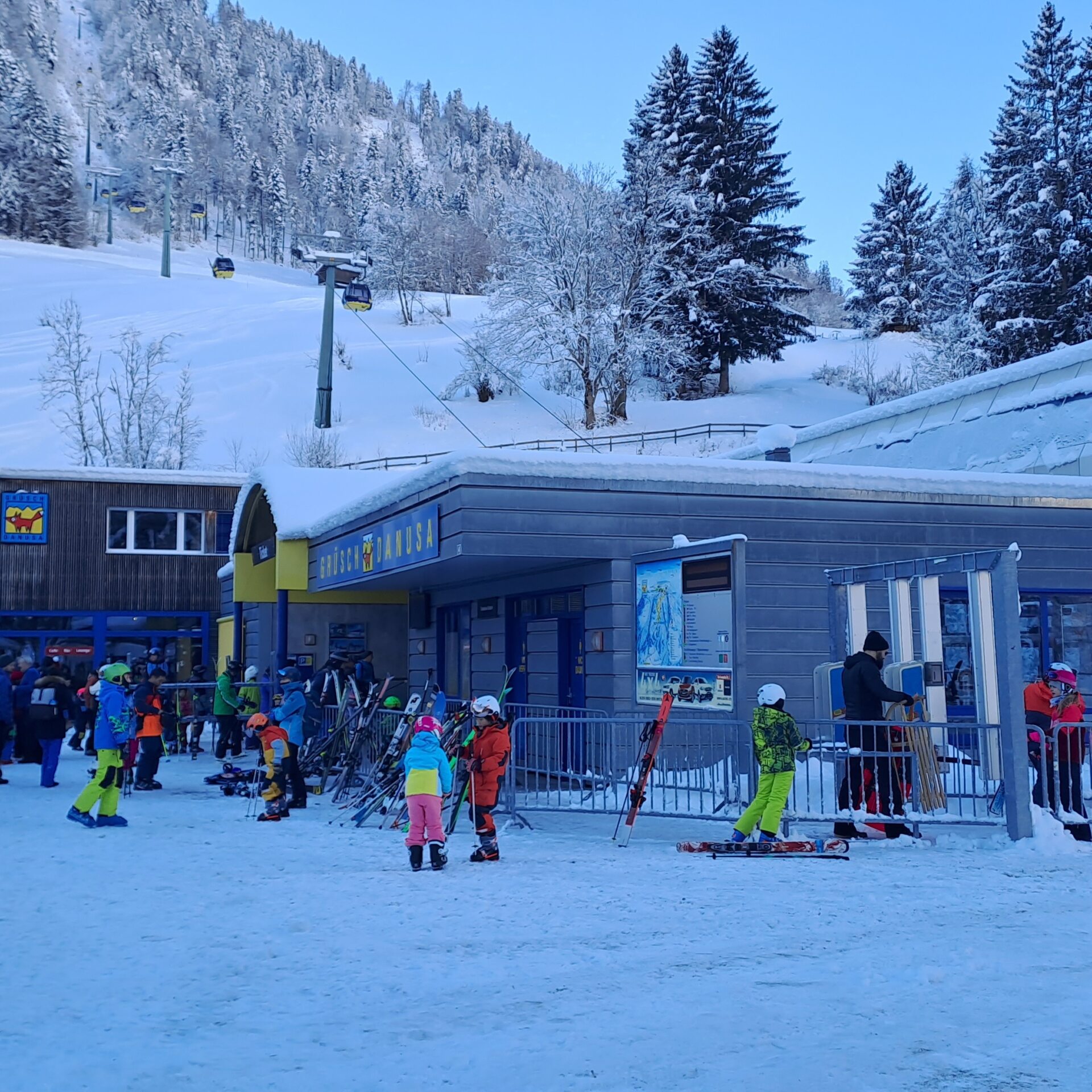 Talstation mit vielen Leuten und Gondelbahn und Gebäude im Hintergrund