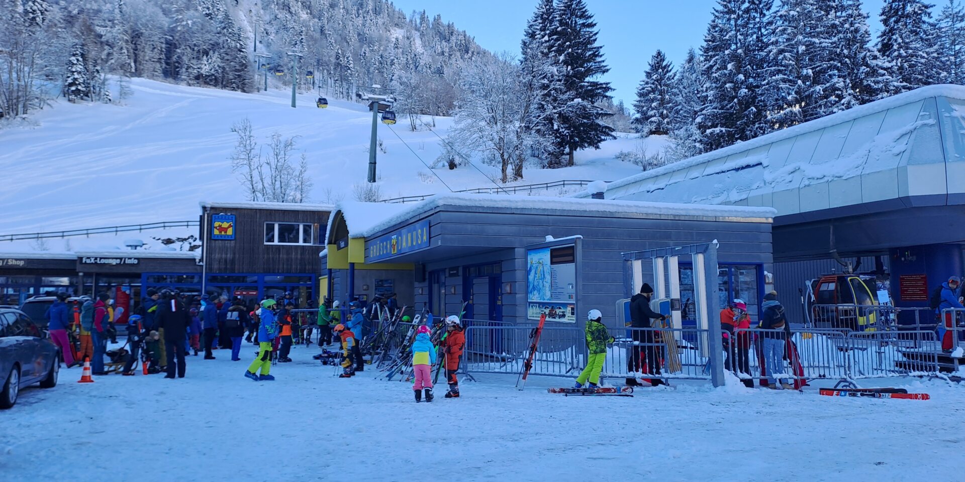 Talstation mit vielen Leuten und Gondelbahn und Gebäude im Hintergrund